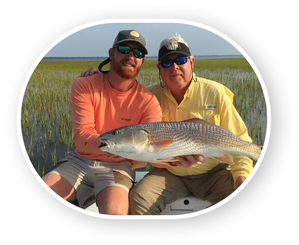 Two anglers holding a redfish in the marsh