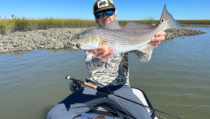Angler holding a redfish near an oyster bar